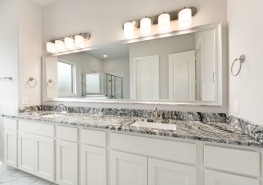 A white bathroom with marble counter tops and a large mirror.