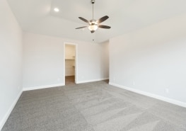 Empty bedroom with gray carpet and ceiling fan.