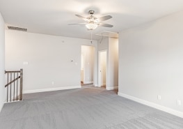 An empty room with gray carpet and a ceiling fan.