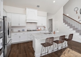 A white kitchen with hardwood floors and a staircase.