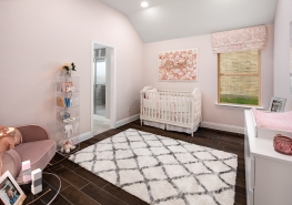 A pink and white nursery with a crib and a rug.
