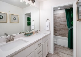 A bathroom with white cabinets and green shower curtain.