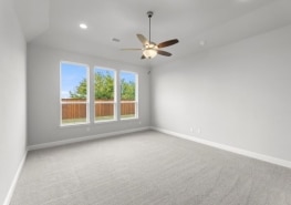 An empty room with a ceiling fan and gray carpet.