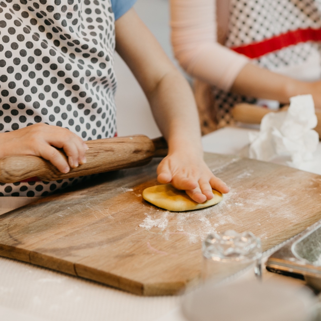 Two children preparing dough on a wooden cutting board.