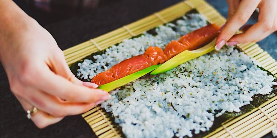 A person cutting salmon on a bamboo mat.
